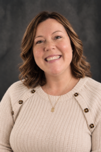 Bree Kibble, Administrative Services Coordinator for the College of Sciences, wearing a ribbed cream shirt with brown buttons at the shoulders, poses in front of a mottled gray background.