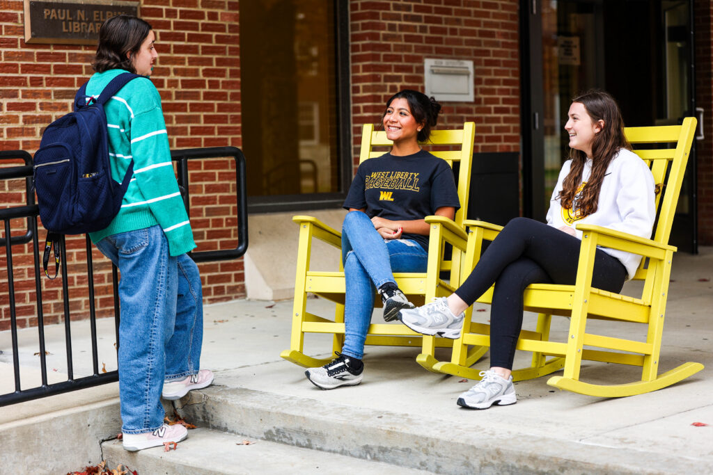 students chatting by campus rocking chairs